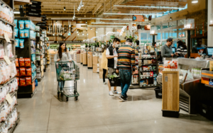 Inside a grocery retailer, at the checkout lines with shoppers in line.