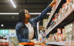 Woman pushing a cart in a grocery store reaching to a shelf to pick up a product - Challenging Legacy Food & Beverage Brands through CPG Marketing