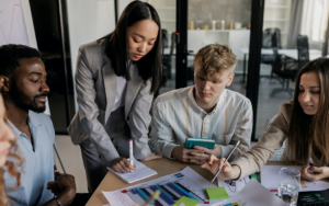 Group of 4 young people around a table discussing business metrics | Budget Cuts? Here's How to Make the Most Out of Your CPG Marketing Budget blog